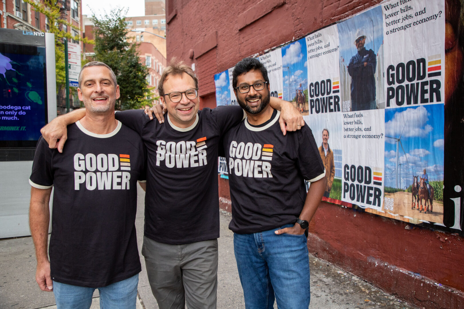 Matt Lukens, Steve Hargreaves, and Rahul Mukherjee stand in New York City in front of wheatpasting advertisements for GoodPower